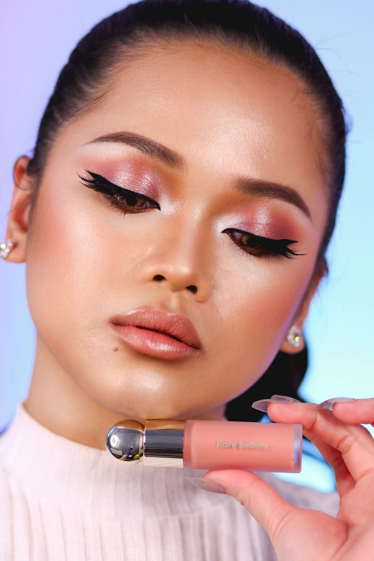 Model with shimmering rose-gold eye makeup holding a lip product